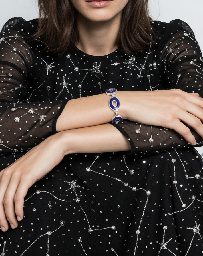 Person wearing a black dress with star constellation patterns and a blue and silver bracelet.